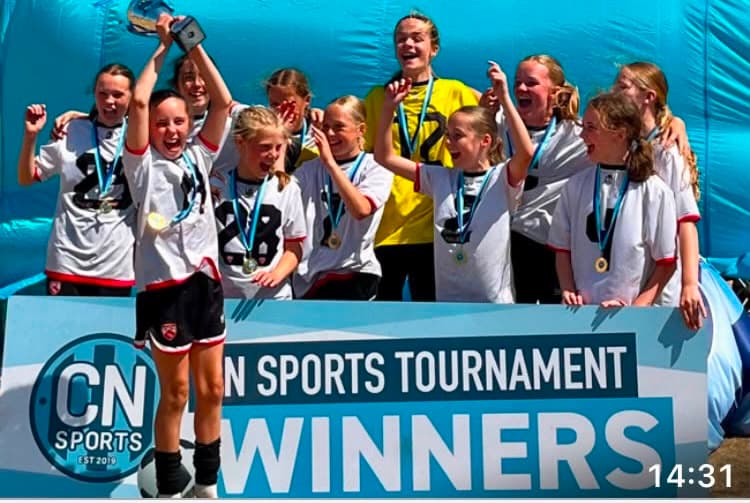 Morecambe Girls FC players celebrating a tournament win with medals and a trophy